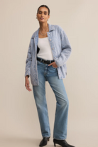 Woman wearing a light blue denim jacket and jeans on a beige background