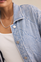 Close-up of a person wearing a light blue denim jacket with a white shirt underneath.