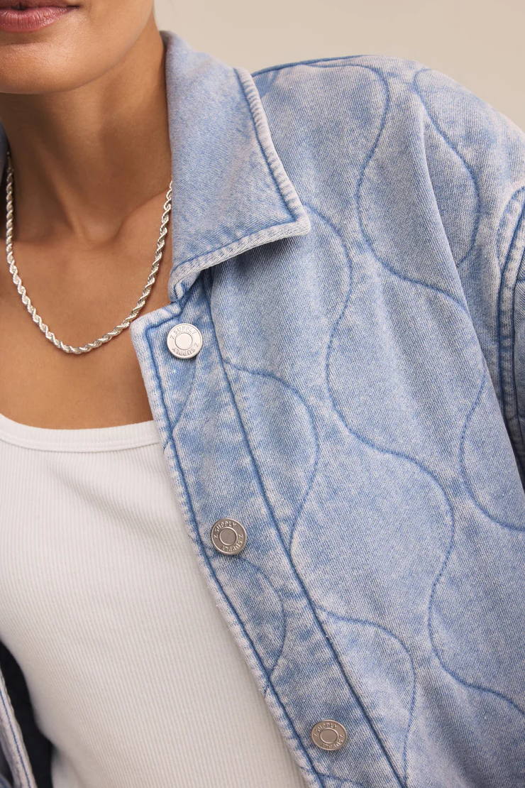 Close-up of a person wearing a light blue denim jacket with a white shirt underneath.