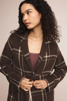 Woman wearing a brown plaid coat against a neutral background