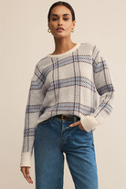 Woman wearing a plaid sweater and blue jeans against a beige background