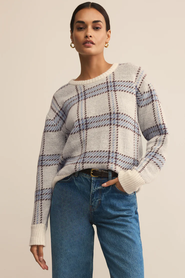 Woman wearing a plaid sweater and blue jeans against a beige background