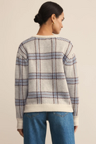 Person wearing a plaid sweater and blue jeans on a beige background