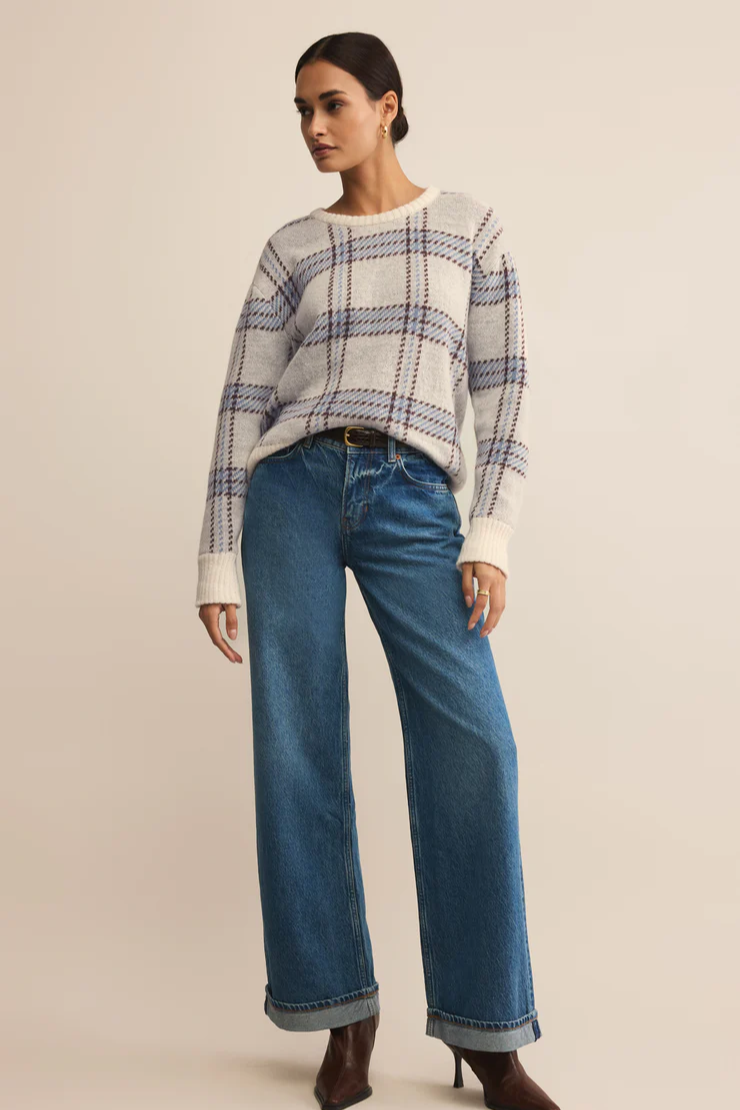 Woman wearing a plaid sweater and blue jeans on a beige background