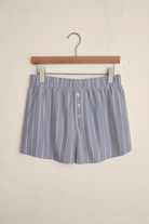 Blue and white striped shorts on a wooden hanger against a beige wall.