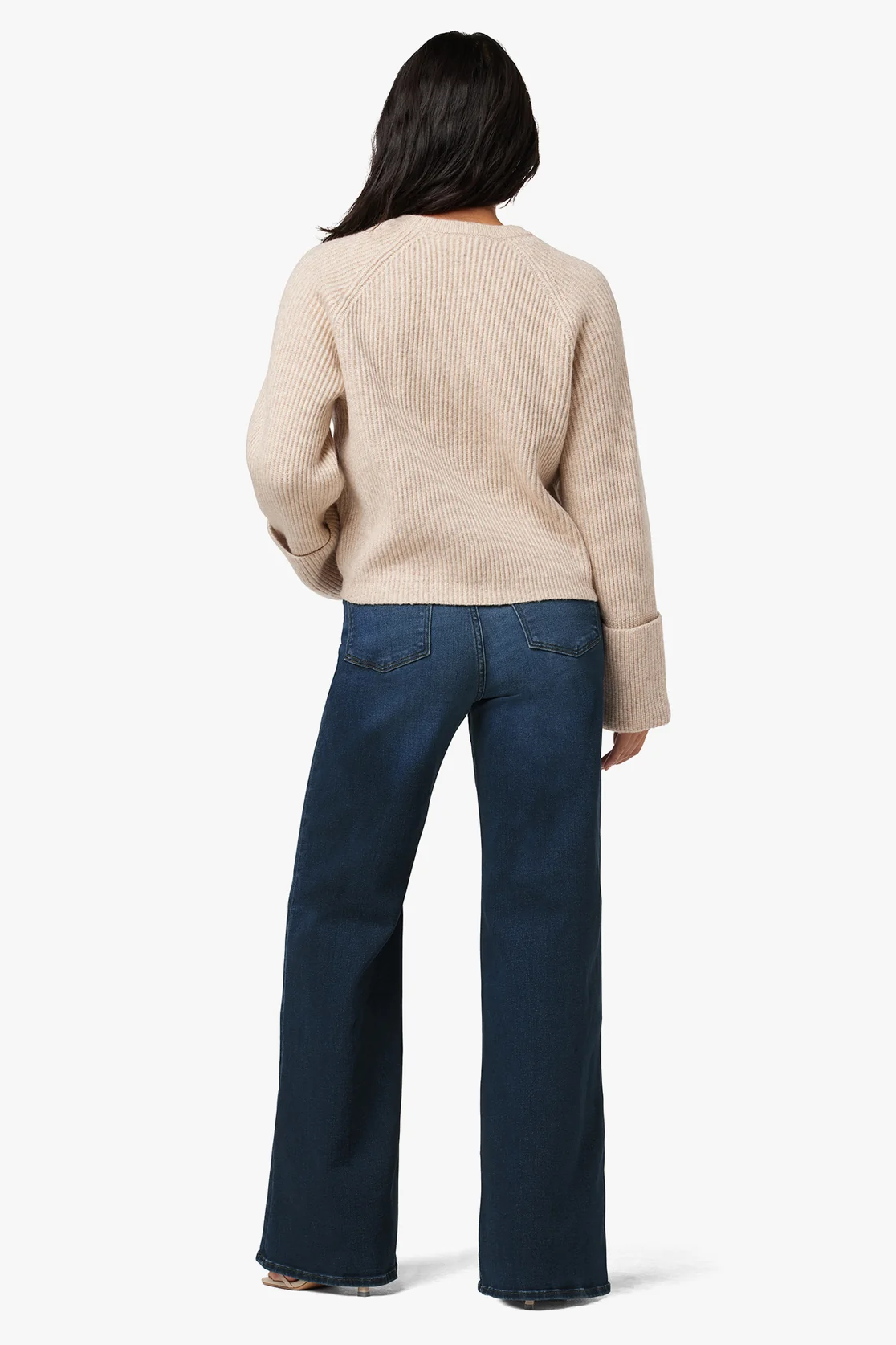 Person wearing a beige sweater and blue jeans on a white background