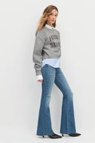 Woman wearing a gray sweatshirt with text, white shirt, and blue flared jeans on a white background