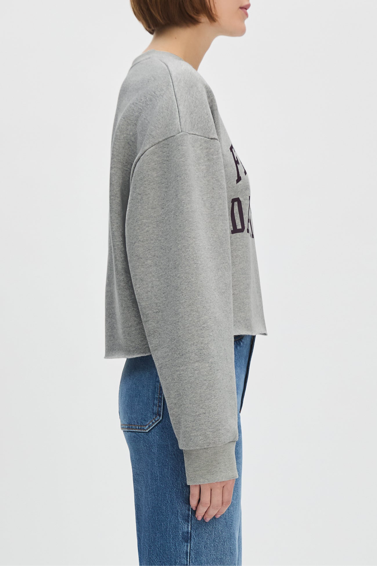 Person wearing a gray sweatshirt with text and blue jeans on a light gray background