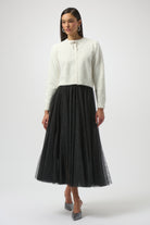 Woman wearing a white cardigan and black tulle skirt on a white background