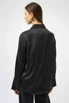 Person wearing a black satin shirt with a textured collar on a white background