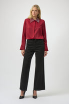 Woman wearing a red blouse with a high collar and black pants on a white background