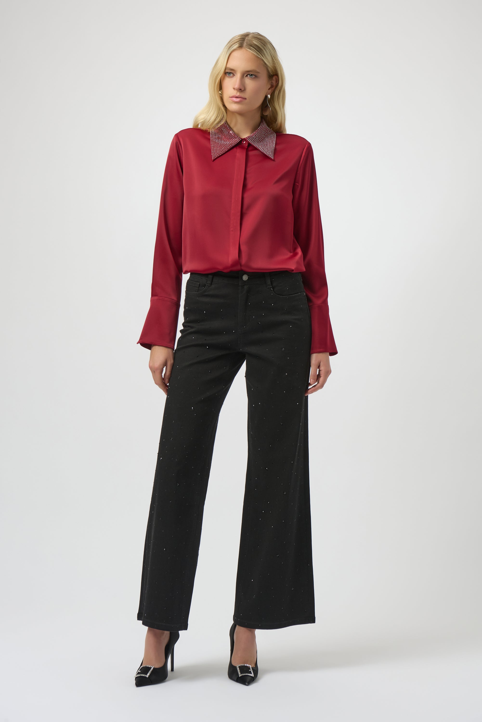 Woman wearing a red blouse with a high collar and black pants on a white background