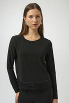 Woman wearing a black long-sleeve top with fringe details on a white background