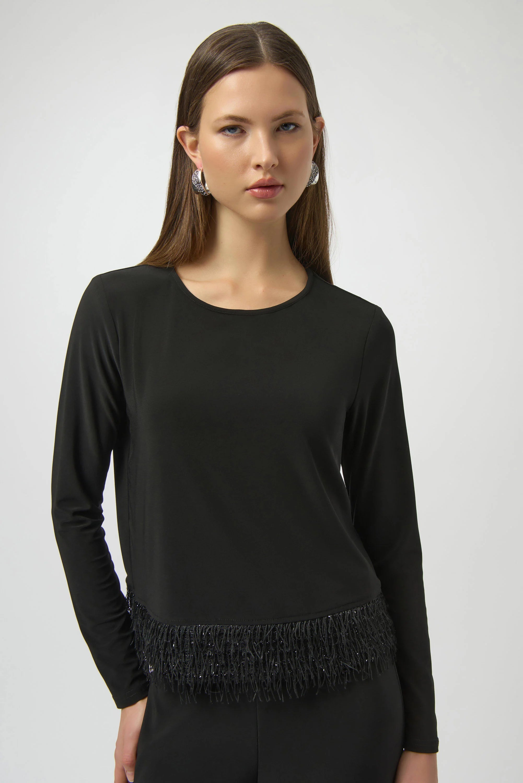 Woman wearing a black long-sleeve top with fringe details on a white background