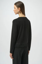 Woman wearing a black long-sleeve top with fringe details on a white background