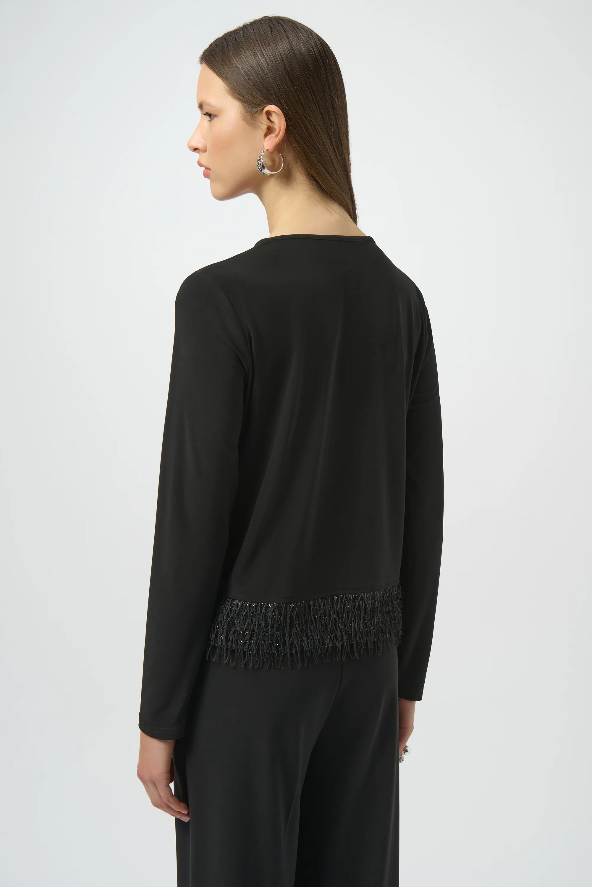 Woman wearing a black long-sleeve top with fringe details on a white background