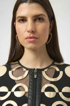Woman wearing a black and gold patterned top with a plain background
