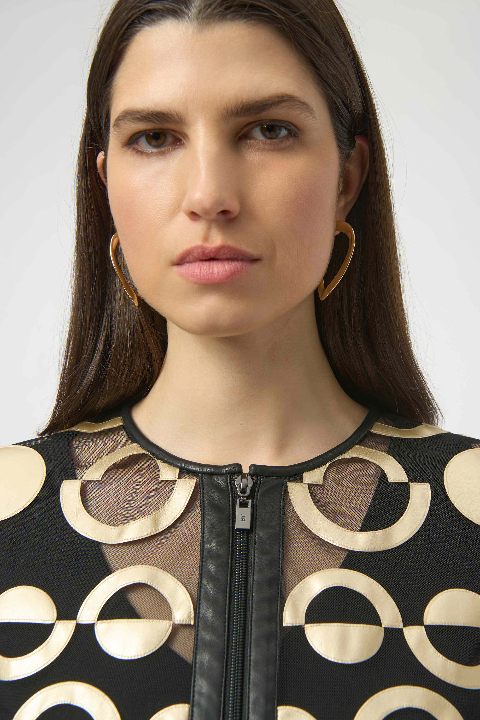 Woman wearing a black and gold patterned top with a plain background