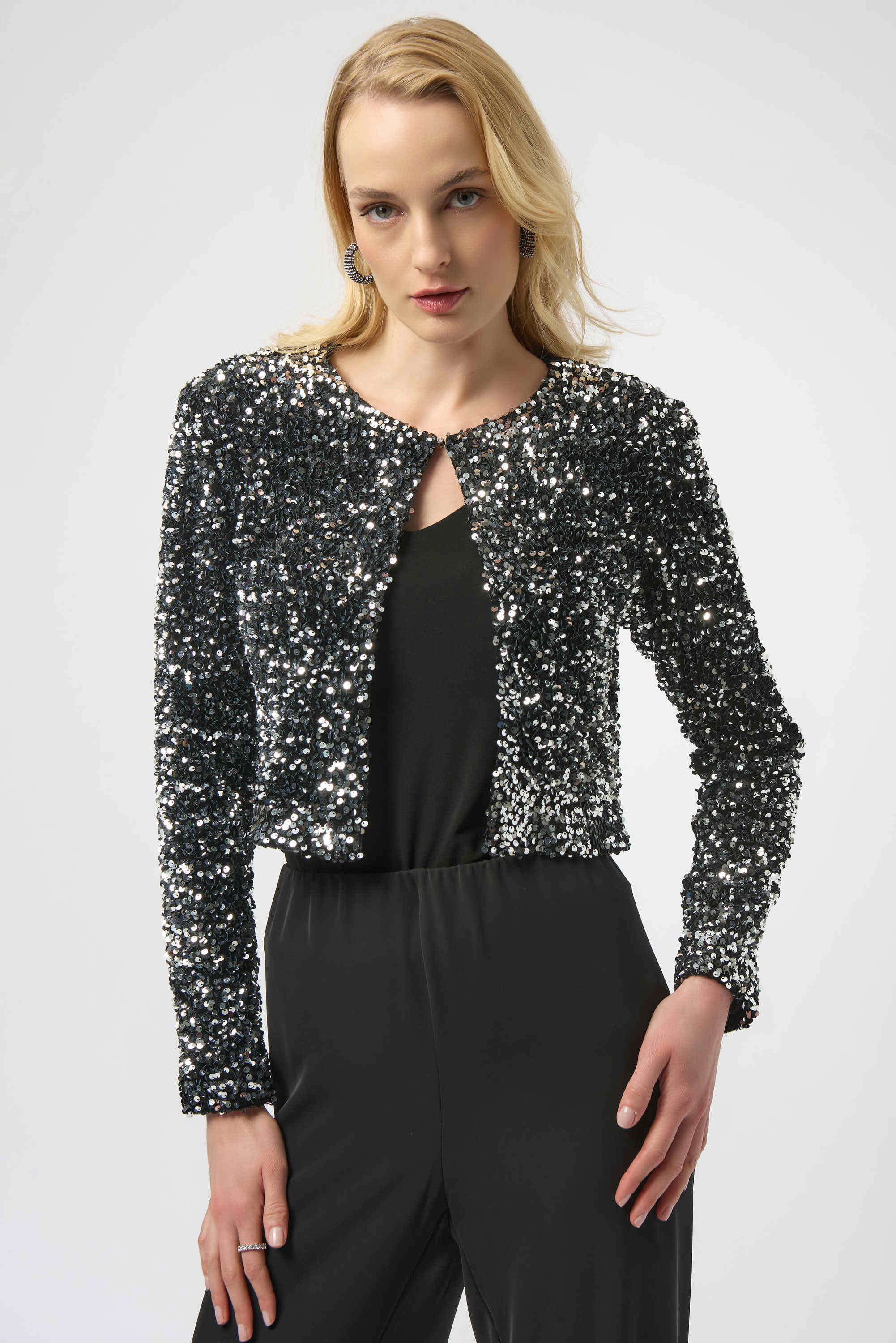 Woman wearing a black sequin jacket over a black top and pants on a white background