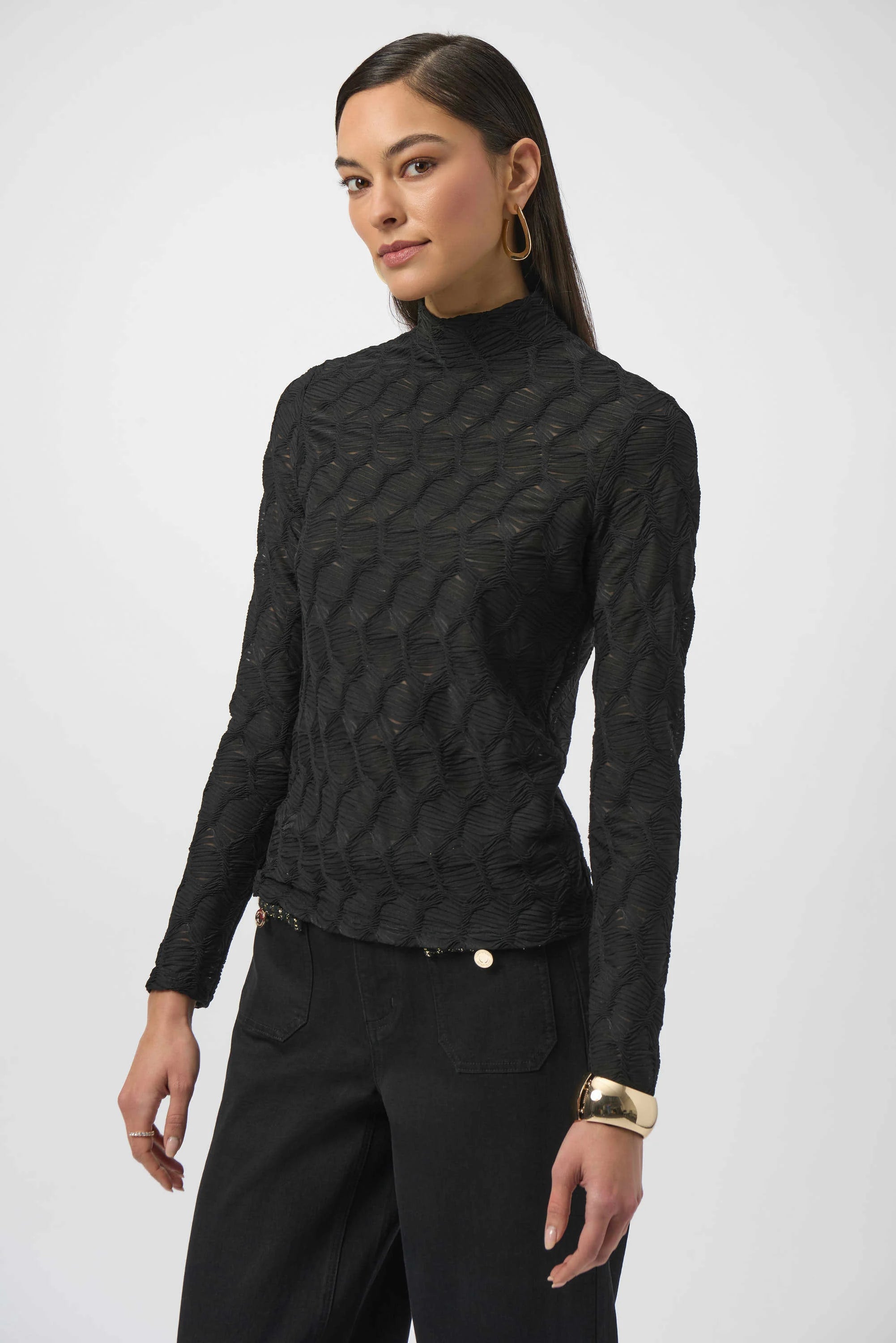 Woman wearing a black textured long-sleeve top and black pants on a white background