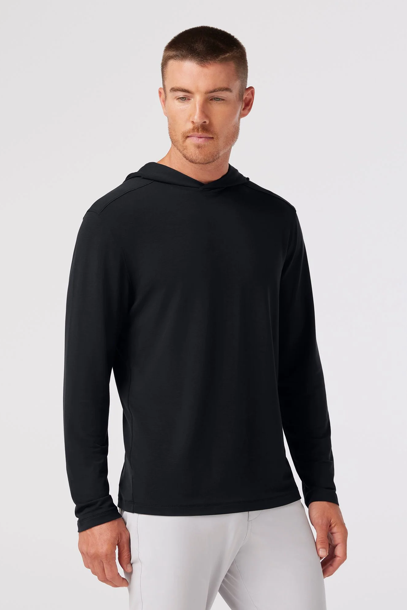 Man wearing a black hoodie and white pants on a light gray background