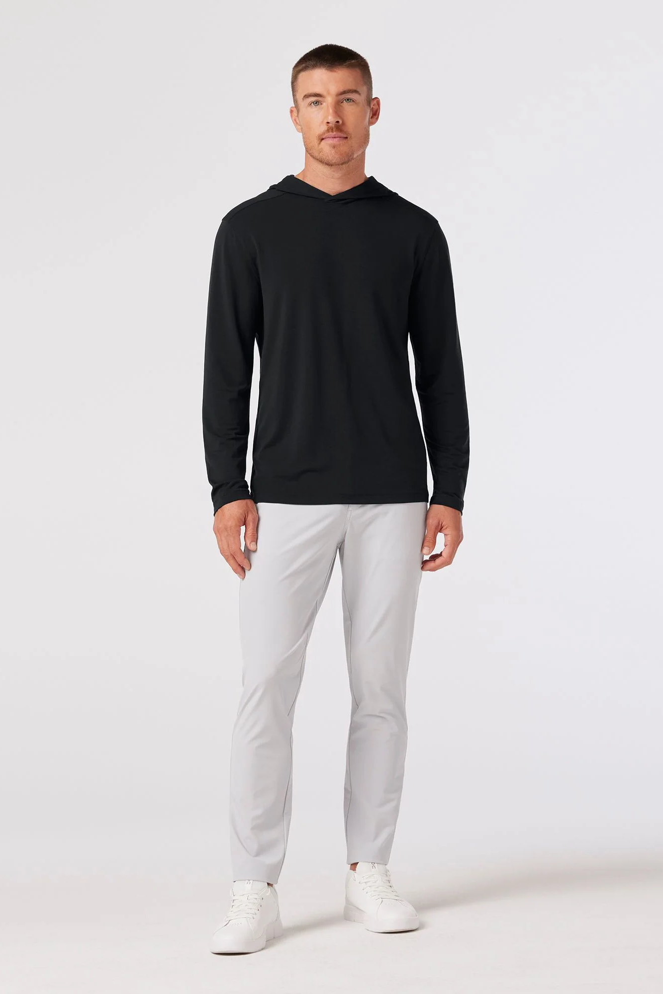 Man wearing a black long-sleeve shirt and white pants on a white background