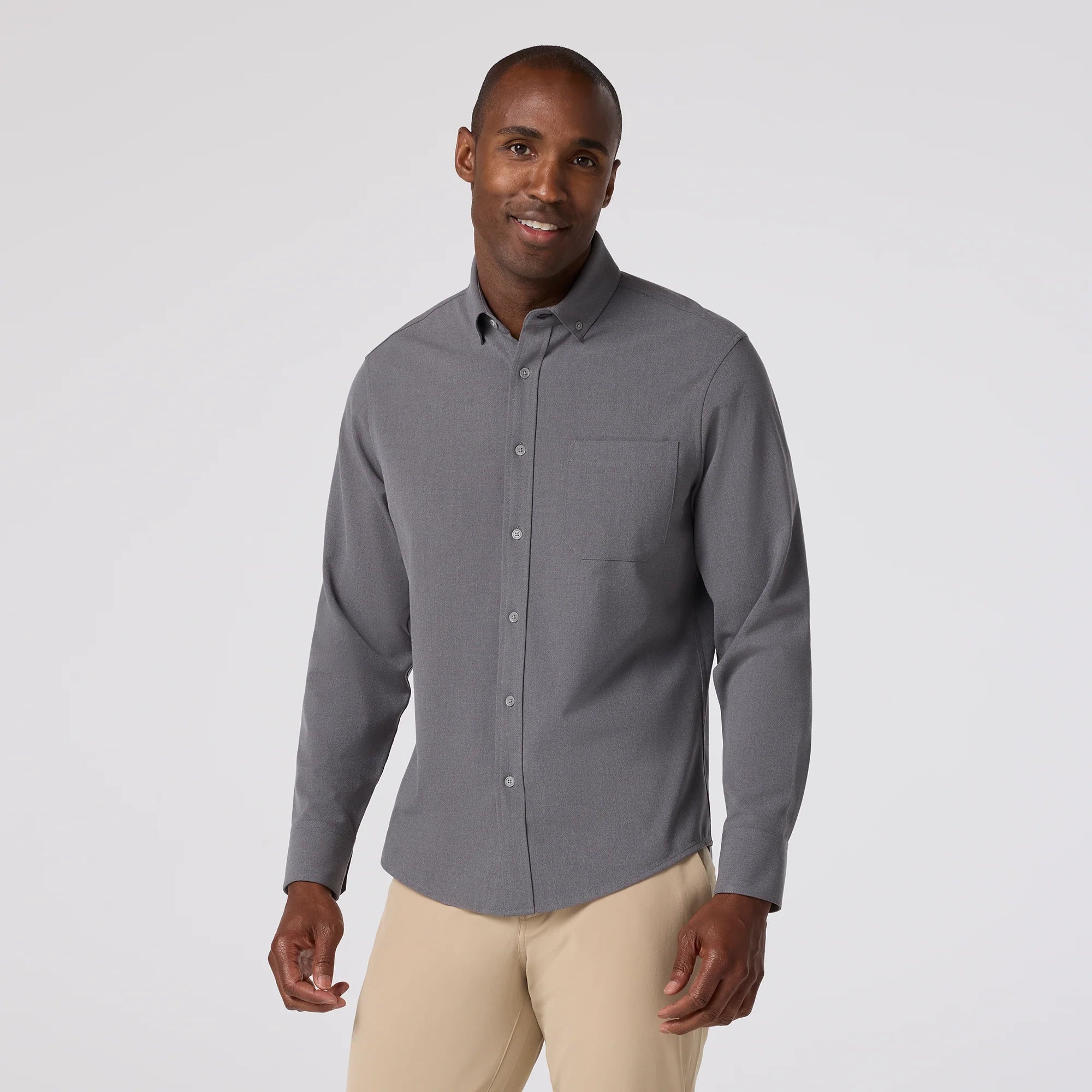 Man wearing a gray button-up shirt and beige pants on a white background