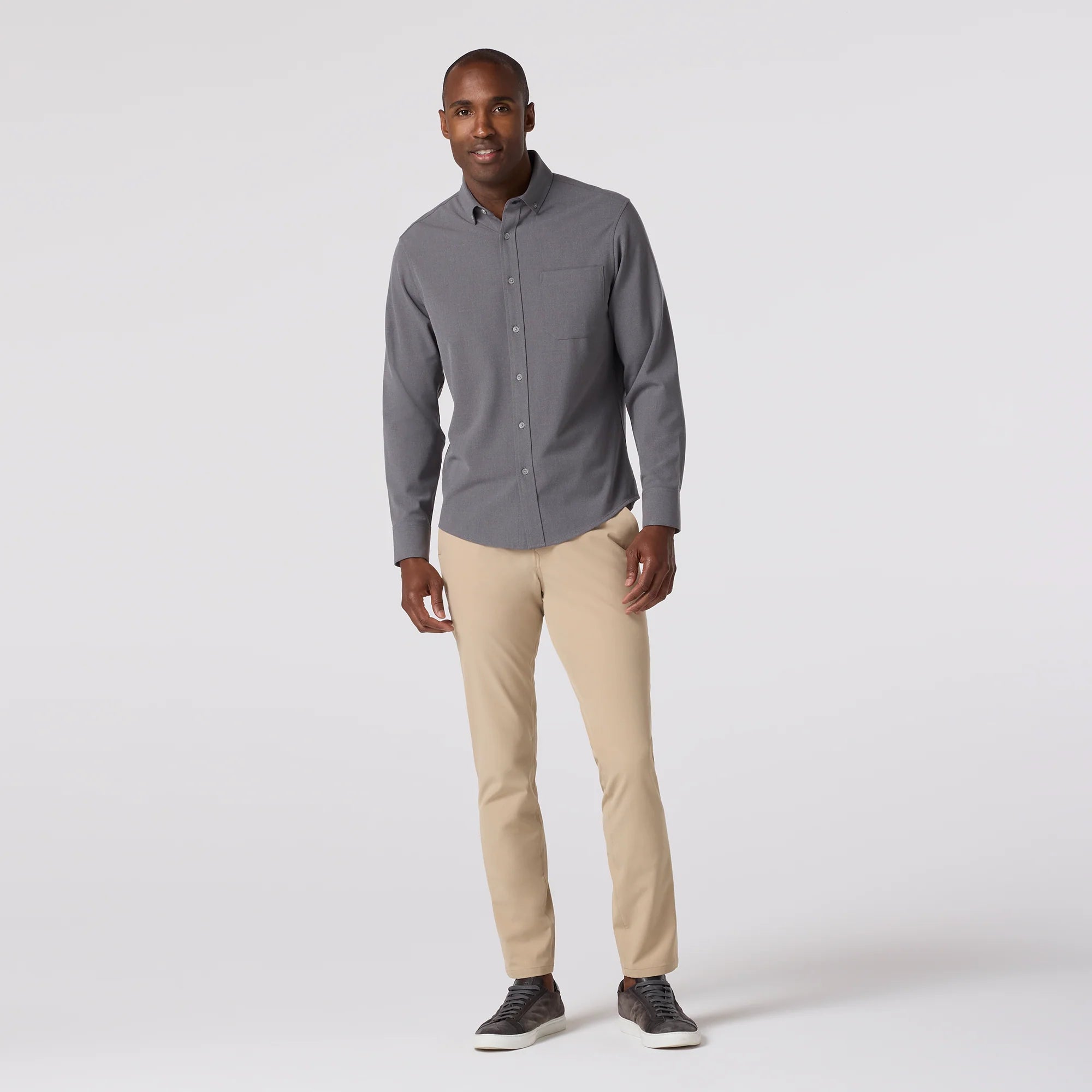 Man wearing a gray button-up shirt and beige pants on a white background