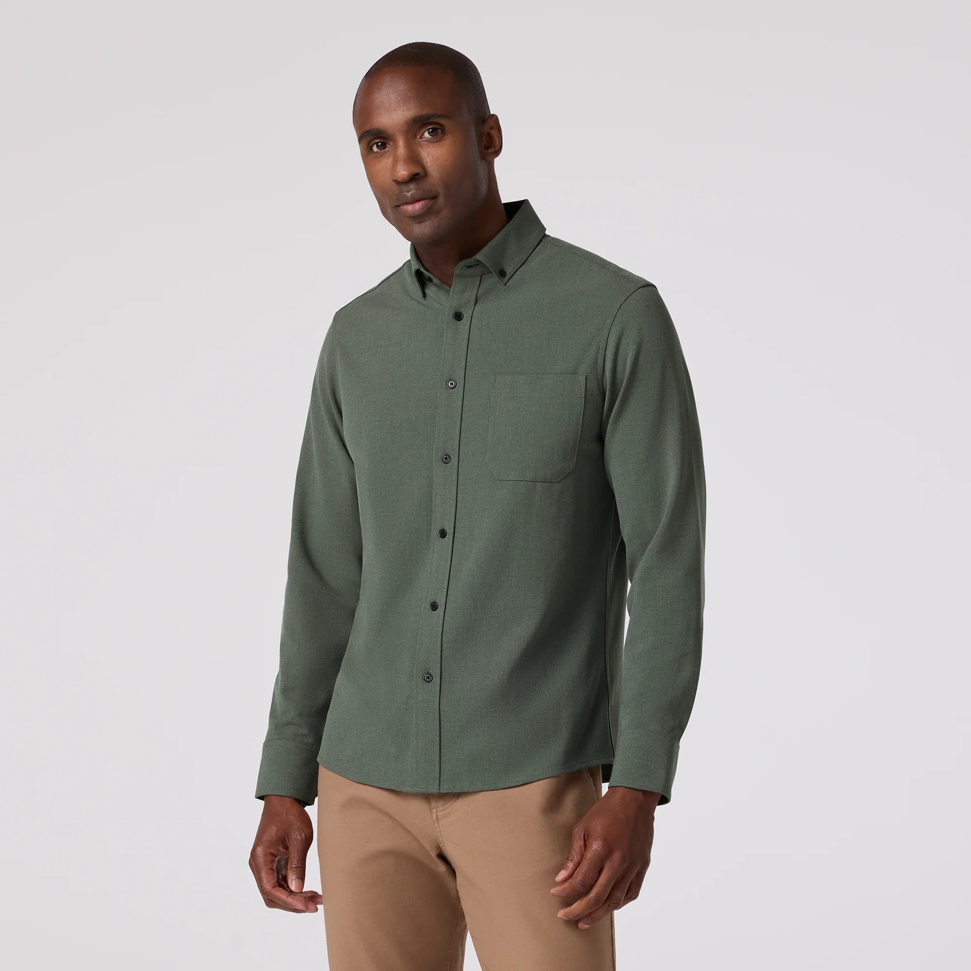 Man wearing a green button-up shirt and beige pants on a white background