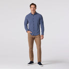 Man wearing a blue checkered shirt and brown pants on a white background