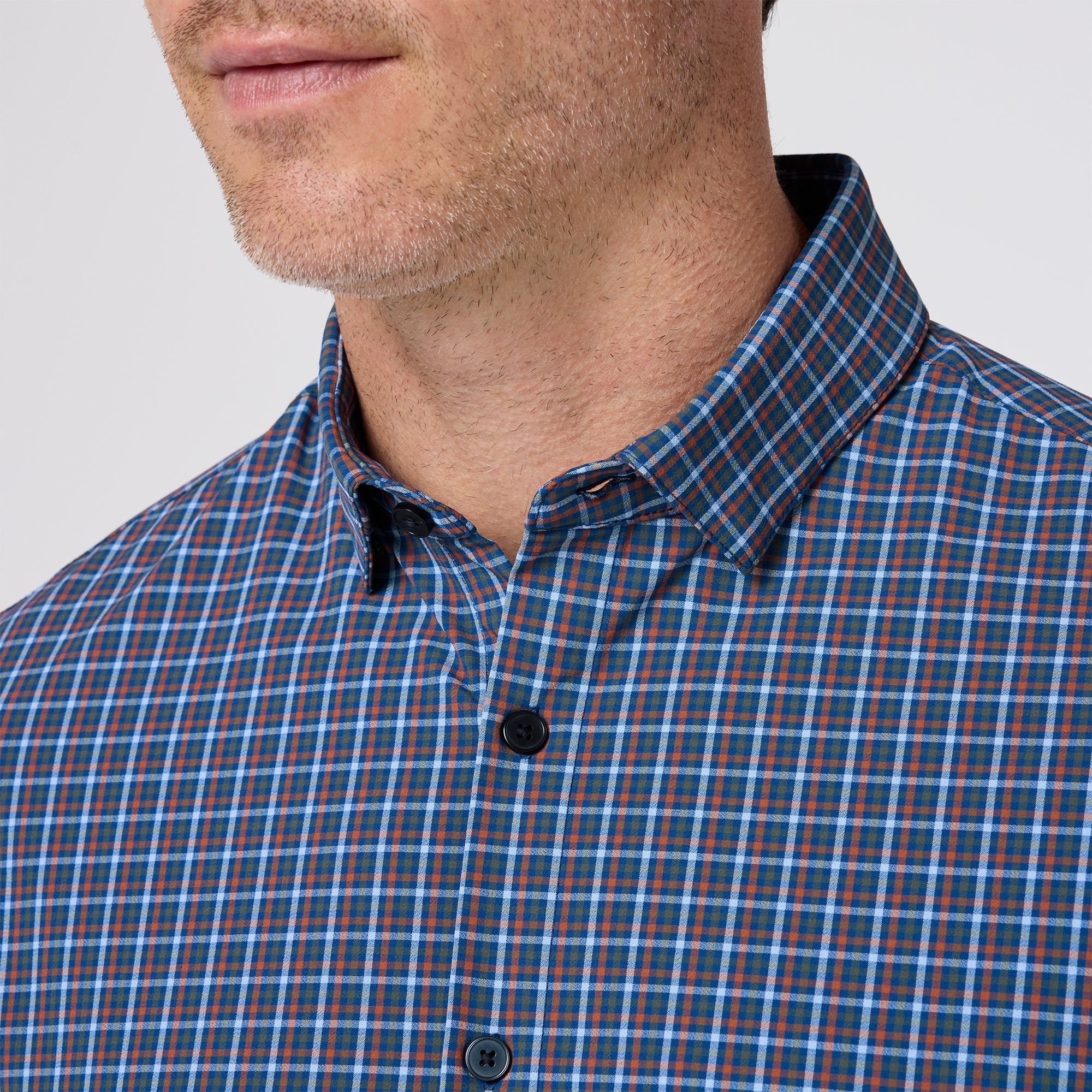 Close-up of a person wearing a blue and orange plaid shirt against a plain background