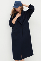 Woman wearing a navy coat and cap against a white background