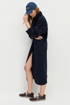 Person wearing a navy blue dress with a high slit, brown sneakers, and a matching cap on a white background