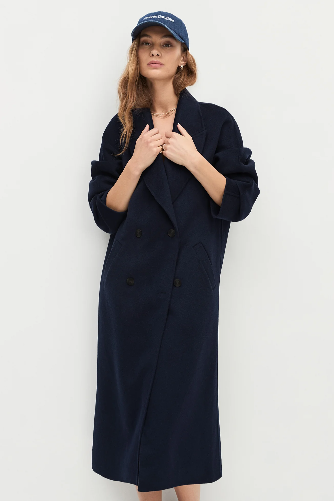 Woman wearing a long navy coat and a blue cap against a white background