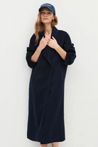 Woman wearing a long navy coat and a blue cap against a white background