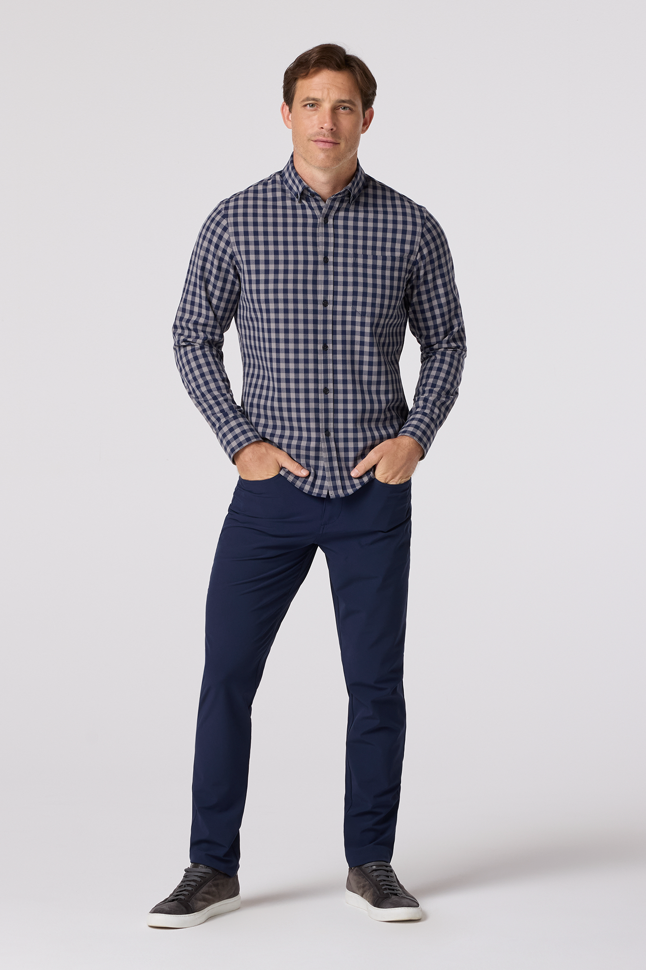Man wearing a blue checkered shirt and navy pants on a white background