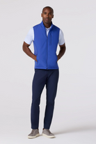 Man wearing a blue vest over a white shirt with navy pants on a white background