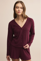 Woman wearing a ribbed burgundy sweater and shorts set against a beige background