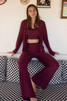 Woman in a burgundy outfit sitting on a checkered couch with a white wall and framed pictures in the background.