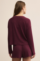 Person wearing a maroon ribbed sweater and shorts set on a beige background