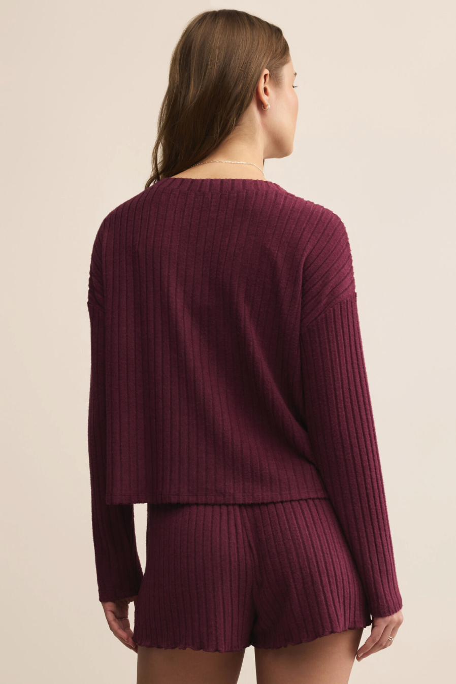 Person wearing a maroon ribbed sweater and shorts set on a beige background