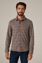 Man wearing a patterned shirt and dark pants against a neutral background