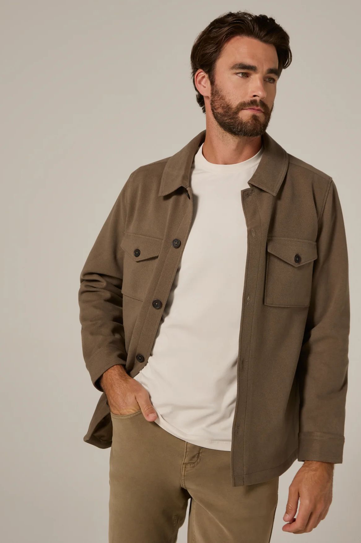 Man wearing a brown jacket over a white shirt on a plain background