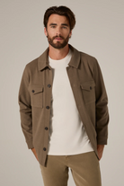 Man wearing a brown jacket over a white shirt with a neutral background