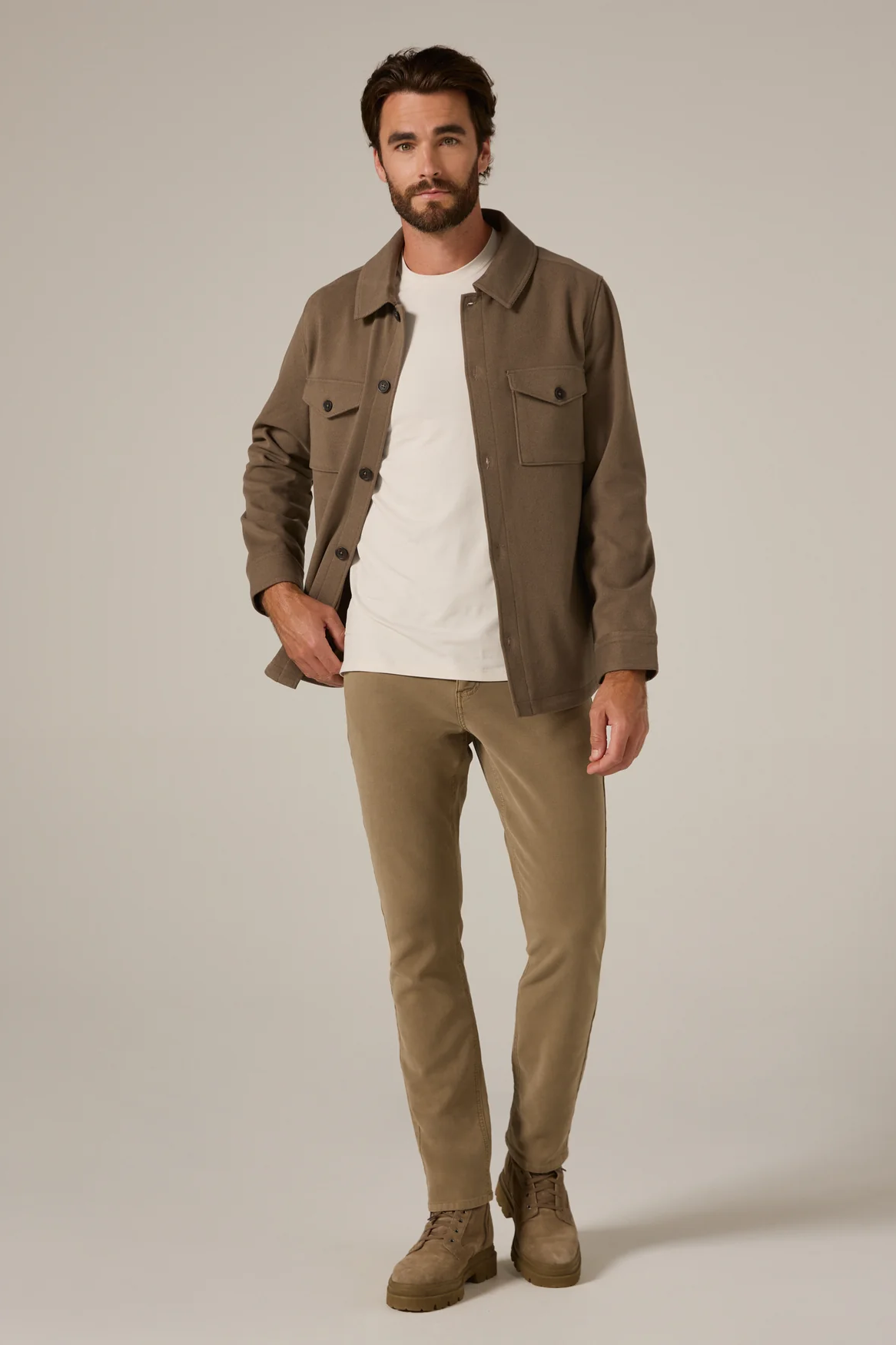 Man wearing a brown jacket, white shirt, and beige pants on a plain background