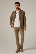 Man wearing a brown jacket, white shirt, and beige pants on a plain background