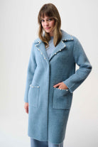 Woman wearing a light blue coat with pearl embellishments on a white background