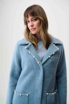 Woman wearing a blue coat with pearl embellishments against a white background