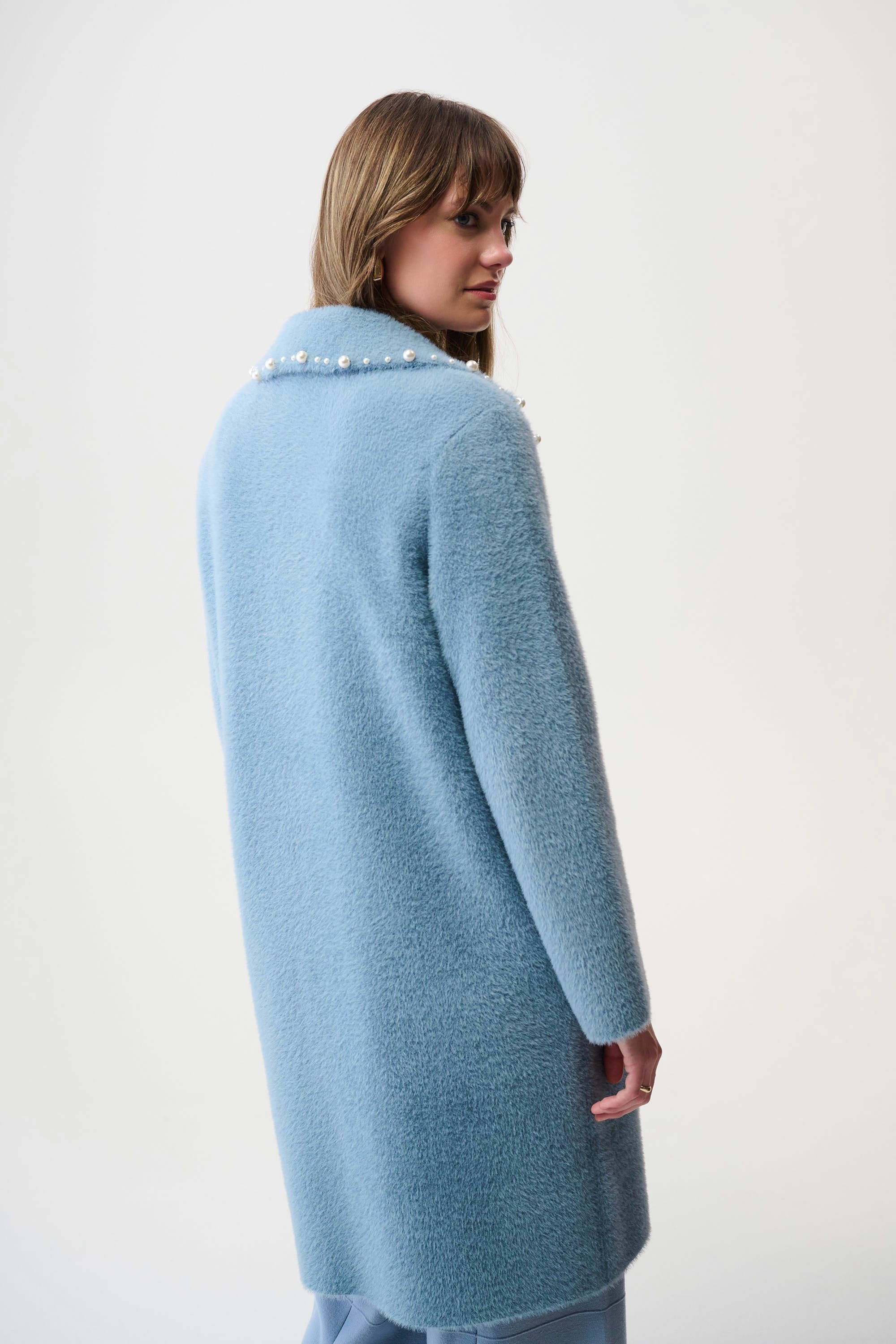 Woman wearing a light blue coat with pearl buttons on a white background