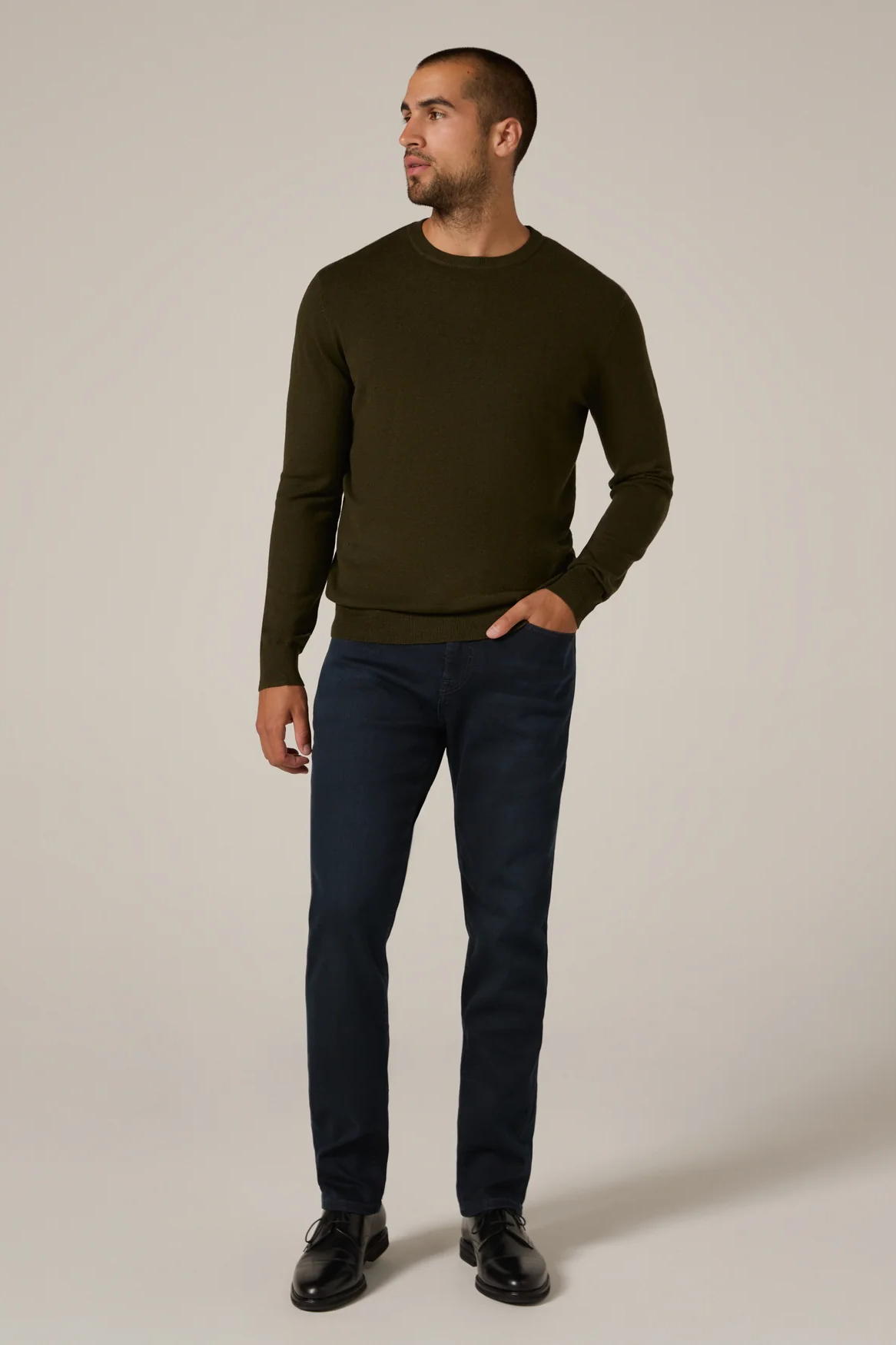 Man wearing a dark green sweater and navy pants on a beige background